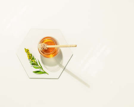 Liquid honey in glass jar, meadow flower and honey dipper on a white table with place for text.の写真素材