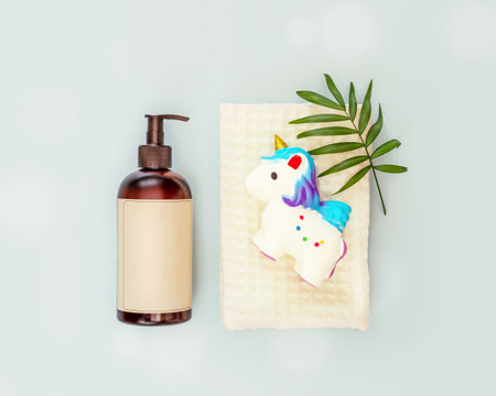Children bathing and baby care. A bottle with baby soap, a white towel, unicorn bath toy and palm leaf on a blue background with bubbles. Baby hygieneの写真素材