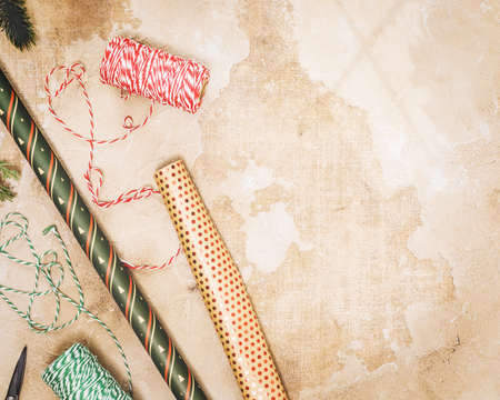 Preparing for the New Year and Christmas, making and decorating gifts. Holiday composition with wrapping paper, festive ribbons, New Year decor and scissors on a textured background with copy spaceの写真素材
