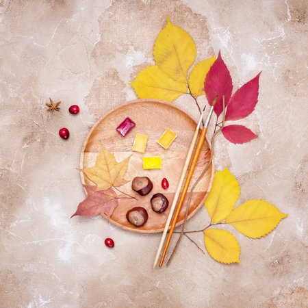 A wooden tray with dry leaves, watercolors, brushes, cranberries and chestnuts