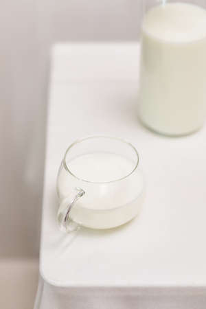 Morning still life with cup of farm milk and bottle on a white tableの写真素材