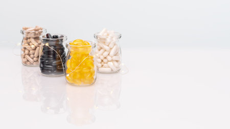 A set of natural vitamin and supplement capsules in glass jars with lighting garland on light...