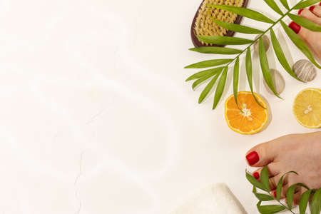 Spa relax composition with well-groomed foot with pedicure, spa accessories, citrus fruits and palm leaves on a white background with copy space. Salon wellness procedure for foot careの写真素材