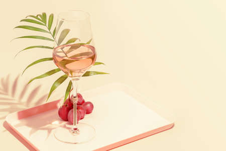 Glass of rose wine with palm leaf and grape on a pink backgroundの写真素材