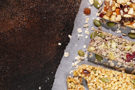 Natural granola cereal bars with nuts, seeds, oats, berries and dry fruits on a dark brown textured background with copy space. Protein muesli bars. Granola superfood. Natural energy healthy snackの写真素材