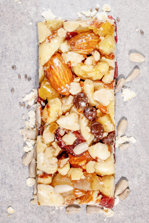 Natural granola cereal bar with nuts, seeds, oats, raisins and honey on a white pergament paper....