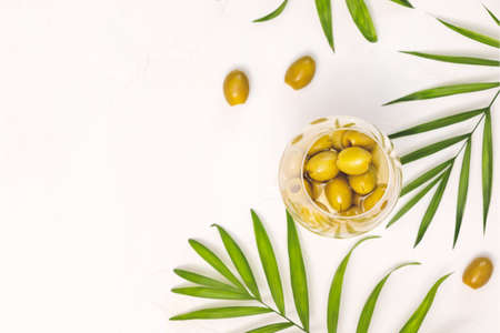 Food composition witn organic green olives in a glass and palm leaves on a white background with palm leaves. Olive season. Mediterranean food. Flat layの写真素材
