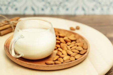 Non diary milk. Vegan food composition with cup of almond milk and almond nuts on a wooden plate and cinnamon sticks on a eco friendly kitchen. Rustic still life with vegan healthy productの写真素材