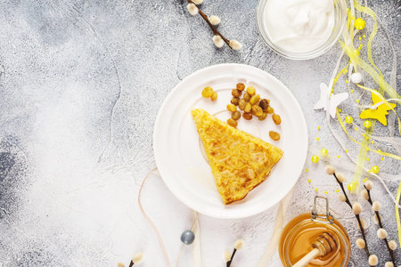 Sweet homemade fried crepe with honey, raisins on a white plate with holiday decoration, sour cream...