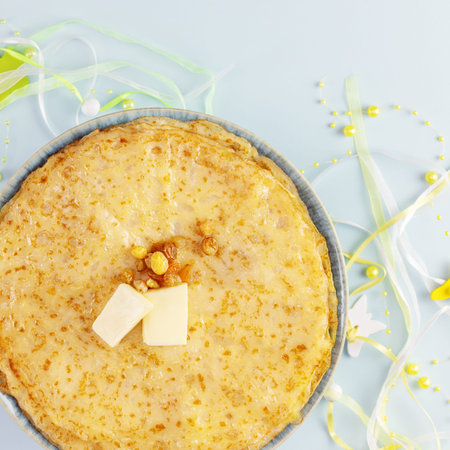 Stack of homemade fried crepes with butter and raisins and holidays decoration on a blue background....