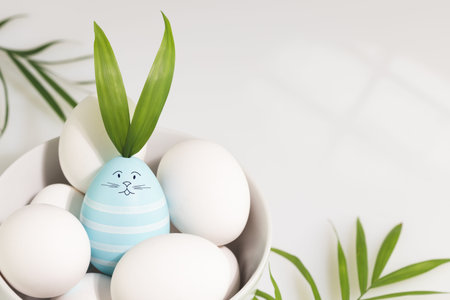 Easter eggs in a white bowl on a white table with palm leaves