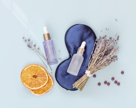 Relax composition with sleep mask, lavender oil and serum with lavender flowers on blue background....
