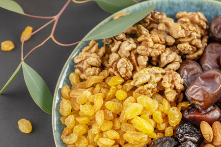 Golden raisins, walnuts, almonds, prunes and dates in the blue bowl on a black background with a...