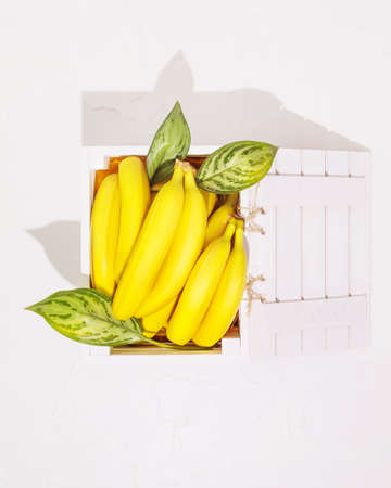 Fresh, ripe bananas with leaves in a white wooden boxの写真素材