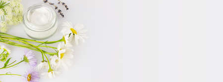 Concept of wild-harvested beauty and natural cosmetics based on a wild plant. Glass jar with organic creams and wild flowers on a white background with copy space. Soft focus style, banner sizeの写真素材