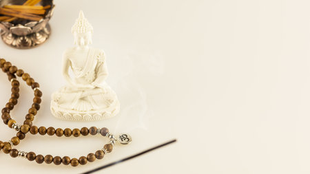 Buddha statue, prayer beads and aroma sticks on a white background with copy space. Asian spa ritual procedure, healing and meditation. Energy health and relaxation. Vesak, Buddha Day. Soft image styleの写真素材
