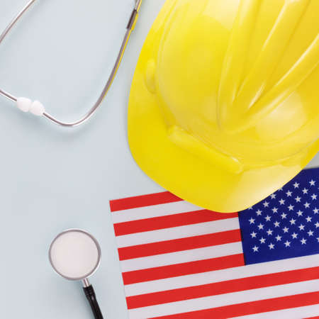 Medical care and insurance of workers in America. American flag, stethoscope and hardhat on a blue background. Labor safety and right at Workplace in United Statesの写真素材