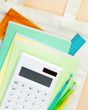 Back to school flat lay with multicolored notebooks, pens, rulers and calculator on a white textile bag. School supplies on a ivory background. School sale and buying concept. Flat lay, closeupの写真素材