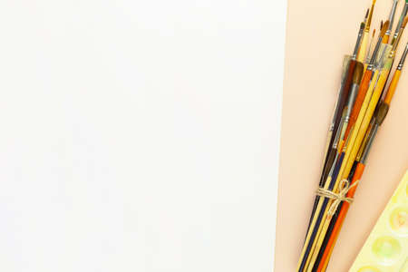 Back to art school background with brushes, palette and empty white sheet of paper. School supplies on a ivory background with copy space. flat layの写真素材