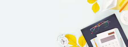 Back to school concept. Banner with School supplies on a tablet with glasses on a blue background with yellow, autumn leaves, alarm clock and copy space. Flat lay, banner sizeの写真素材