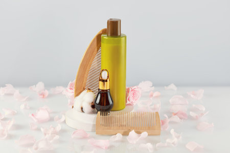 hair cosmetics. mockup. Bottle with beauty product, dropper bottle with natural oil, comb on wooden podium on white table with rose petals. Mock up natural beauty product for hair. Soft image styleの写真素材