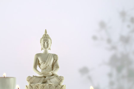 White Buddha statue with candles on a white background with copy spaceの写真素材
