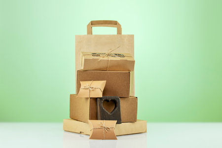 Eco friendly shopping and delivery service. Craft cardboard gift boxes, paper bag and wooden heart on green background. Zero Waste, plastic free, eco packaging concept. Front viewの写真素材