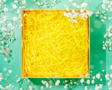 Opened gift box with shredded paper with white flowers. Yellow paper box with decorative straws...