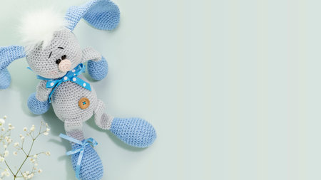 Handmade crochet rabbit toy on blue background with white flowers and copy space. Handmade Easter Bunny Soft Toysの写真素材