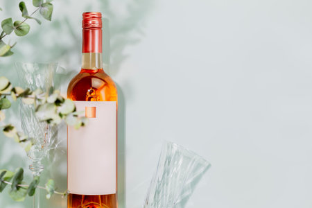 Organic rose wine. Bottle of natural pink wine with wine glasses on blue background with eucalyptus leaves. Summer romantic still life with bottle of low alcohol beverage. Mockup, flat lay, copy spaceの写真素材