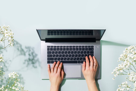 Romantic Overhead shot of womans hands working on laptop on blue background with white spring...