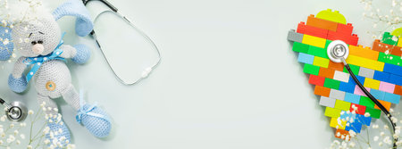 Kids health care banner. Cute knitted toy rabbit and constructor heart with stethoscope on blue background with white flowers. Family doctor or pediatrician concept. Banner size, flat lay, copy spaceの写真素材