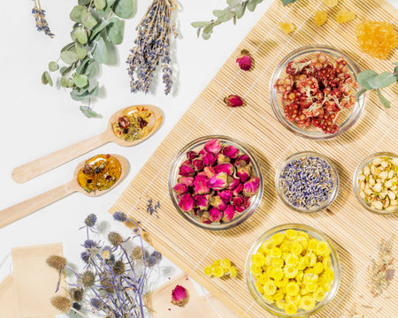 Home herbal apothecary concept. Sustainable flat lay with dry flowers and herbs, tea bags and wooden spoons on wooden napkin on white background. Healing tea from wild plants and flowers.の写真素材
