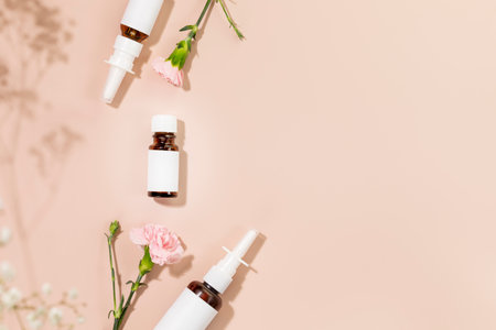 Natural nasal drops, moisturizing spray and oil for treatment of colds and nasal cavity care. Medicine bottles with natural remedies on pink background with flowers. Mock up, flat lay, copy spaceの写真素材