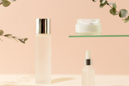 Cosmetic glass jars with natural cream, face serum and organic tonic on pink background with eucalyptus sprigs. Organic beauty product and skin friendly cosmetics concept. Mockup, front viewの写真素材