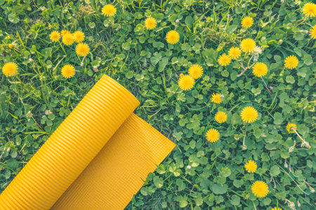 Healthy sport lifestyle background with yellow yoga mat on grass with dandelions. Mat for yoga, meditation, pilates or fitness. Concept of health, sport, summer outdoor activities. Copy spaceの素材