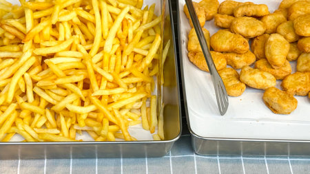 Crispy french fries and golden chicken nuggets are displayed in metal trays, ready for quick service...