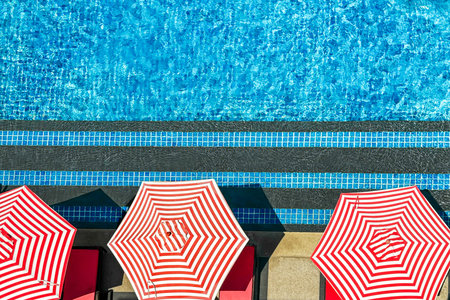 Red and white striped umbrellas along sparkling pool embody resort luxury, offering idyllic escape...