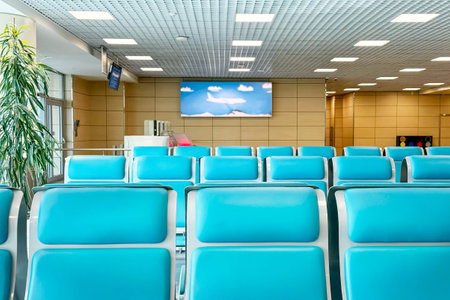 Bright and airy airport lounge with rows of turquoise seats arranged neatly. In background, large...