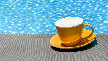 Sunny yellow cup of frothy cappuccino beside vibrant blue tiled poo