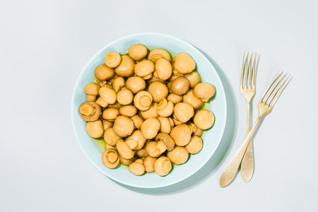 Pickled champignons. Salted, fermented mushrooms on light blue plate, accompanied by vintage forks, highlighting traditional delicacy. Concept of fermented foods, rich in probiotics and rustic flavorsの写真素材