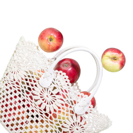Isolated red apples spilling from crocheted bag on white background, highlighting natural, seasonal...