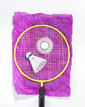 Badminton racket and two shuttlecocks placed on crumpled purple paper, showcasing vibrant and...