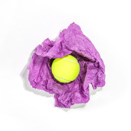 Yellow tennis ball nestled in crumpled purple paper against white background, creating bold contrast and playful vibe. Perfect for promoting tennis events, sports equipment, or active lifestylesの写真素材