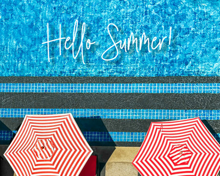 Red striped umbrellas by poolside with mosaic water and Hello Summer text above. Concept of summer vacation, bold patterns, sunny leisure, and vibrant travel visuals for seasonal promosの写真素材