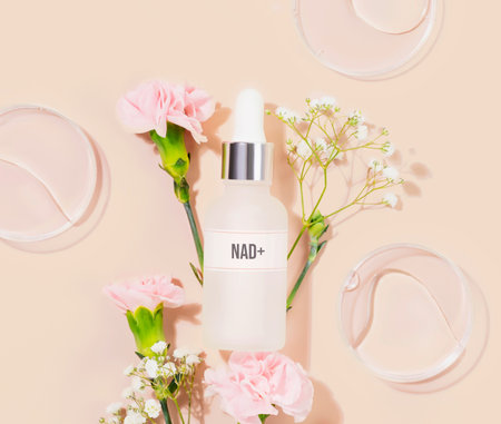 NAD essence in glass droplet bottle surrounded by pink carnations on soft pink pastel background. Concept of NAD beauty products, cellular beauty, anti-aging trends, and modern wellness productsの写真素材