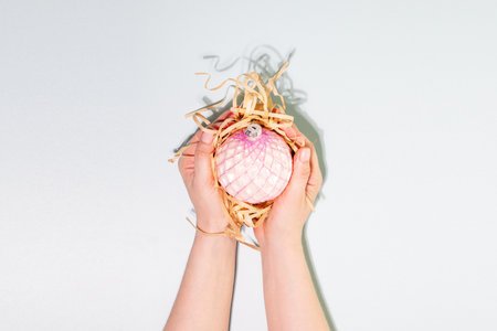 Hands Holding Delicate Pink Christmas Ornament In Eco-Friendly Packaging With Straw Fillerの写真素材