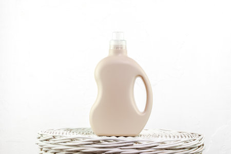 Beige Laundry Detergent Bottle Standing On Wicker Surface Against White Background In Soft Light. Concept Of Sustainable Packaging, Home Care Trends, And Ideal Mockup For Label Design Projectsの写真素材