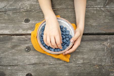 Child s Hands Holding Fresh Blueberries Outdoors On Rustic Wooden Table During Summer Picnic. Concept Of Organic Food, Healthy Eating Habits For Kids, And Nature-Inspired Lifestyle Visualsの写真素材