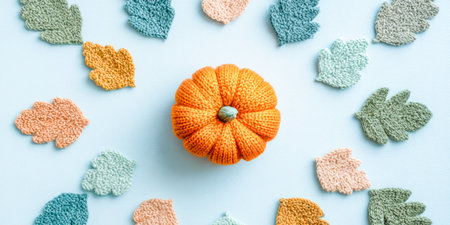 Knitted Pumpkin Surrounded By Soft Colorful Leaves On Light Blue Background. Concept Of Cozy Autumn Decor, Handmade Crafts, DIY, Seasonal Aesthetics, And Fall-Themed Visuals For Home Brandsの素材
